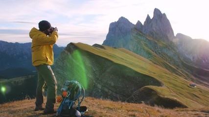 Wall Mural - young man hiker taking pictures at seceda mountain peak at sunrise. backpack, yellow jacket, boots, 