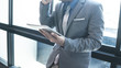 © OMEGA - Businessman using tablet, standing near the window at office.
