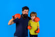 © Svitlana - Sportswear fashion. Parenthood relationship. Bearded sports man coaching boxing little boy in red boxing gloves. Little boy sportsman at boxing training with coach on boxing ring. Ready for sparring.