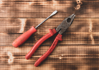 Pliers and screwdriver on a wooden background