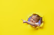 Leinwandbild Motiv Little surprised child looking, peeping through the bright yellow paper hole. Showing hand to side. Advertise childrens goods. Copy space for text.