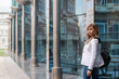 © Марина Демешко - A european beautiful young businesswoman in a white jacket is standing against the background of a mirrored blue business centre, the prospect of the pillars. Dressed in business style
