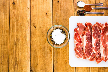 Pork chops with condiments on a white cutting board over wooden table, meat for bbq, top view, copy space, barbeque concept