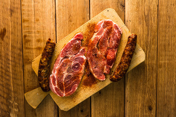 Pork chops with condiments and smoked sausage on a wooden cutting board over wooden table, meat for bbq, top view, copy space, barbeque concept