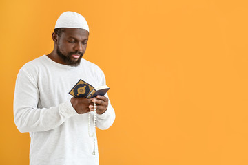 Wall Mural - African-American Muslim man with Koran and beads on color background