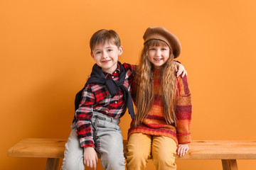 Sticker - Cute little children in autumn clothes sitting on bench near color wall