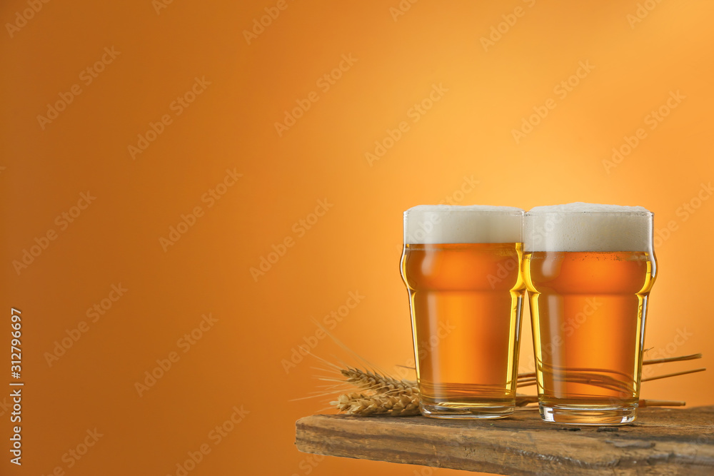 Glasses of beer on table against color background