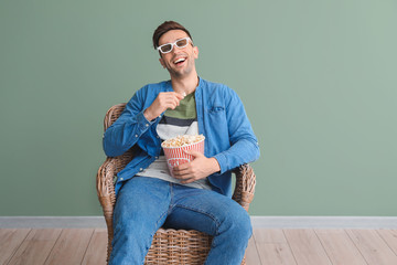 Wall Mural - Handsome man watching movie while sitting in armchair near color wall