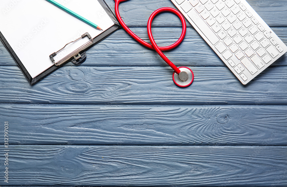 Stethoscope, PC keyboard and clipboard on wooden background