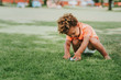 © annanahabed - Cute african toddler boy playing outside with toy cars in the park on green grass, wearing orange polo t-shirt