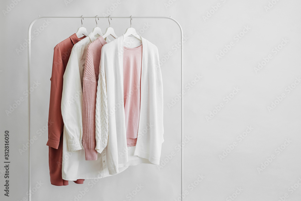 Feminine clothes in pastel pink  color on hanger on white background.  Elegant dress,  jumper, shirt and other fashion outfit. Spring cleaning home wardrobe. Minimal concept. - obrazy, fototapety, plakaty 