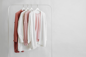 Wall Mural - Feminine clothes in pastel pink color on hanger on white background. Elegant dress, jumper, shirt and other fashion outfit. Spring cleaning home wardrobe. Minimal concept.