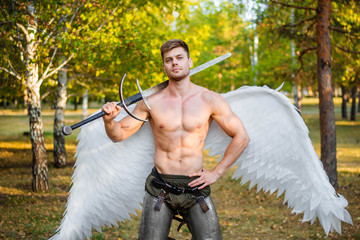 A young angel, a bodybuilder in plate armor on his legs with wings behind his back, holds in his hands a two-handed sword.