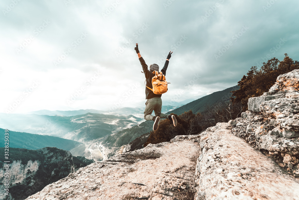 Young man traveler jumps on a background of mountain raising arms to the sky - obrazy, fototapety, plakaty 