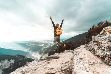 Wall Mural - Young man traveler jumps on a background of mountain raising arms to the sky