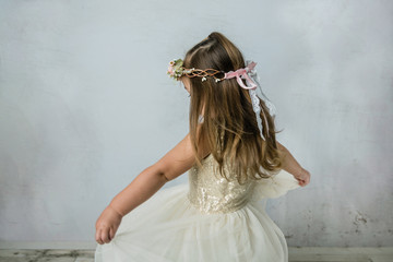 pretty preschool age girl wearing a gold sequined dress and a floral crown spinning and twirling in a pale neutral room. She is happy and having fun playing.