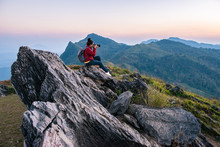 Tourist Woman Take A Photographs Of Beautiful Landscape Of Doi Pha Tang In Chiang Rai Province Of Thailand At Sunset. Doi Pha Tang Is A Mountain Cliff Over Thai-Laotian Border.