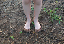 Kid Bare Foot With Muddy Feet On The Rural Road.