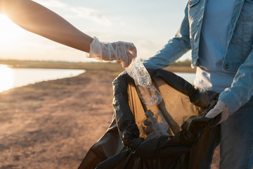 Wall Mural - people volunteer keeping garbage plastic bottle into black bag at park near river in sunset