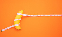 Yellow Banana With Measurement Tape On Orange Background. Men Penis Size Concept With Empty Free Space For Text Or Design