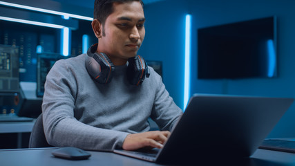 Fototapete - Portrait of Software Developer / Hacker / Programmer Sitting at His Desk and Working on Laptop Computer In the Background Dark Neon High Tech Environment with Multiple Displays. 