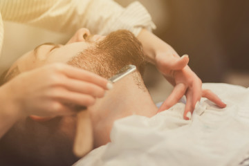 Barber woman shaving client with cut throat razor