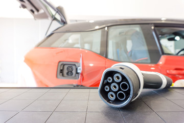 Wall Mural - Electric Car Charger, EV Charging Cable Cord type 2 on blurred electric car on background. Electric car ev type 2 connector charger on blurred electric car on background.