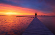 canvas print picture - A man enjoying the colorful  dawn on a jetty in a lake. Groningen, Holland.