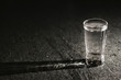 Transparent glass vodka shot on black bar. Empty copy space dark sad alcoholism background.