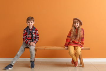 Wall Mural - Cute little children in autumn clothes sitting on bench near color wall