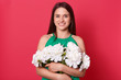 © sementsova321 - Horizontal studio shot of cute cheerful positive young brunette looking directly at camera, holding bouquet of white flowers, standing isolated over red background in studio. Present concept.