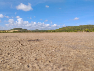 Panoramic photo of dry salt pans of ocher color. Blue sky with tropical clouds and mountains with vegetation. Martinique, French West Indies.