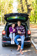 © F8  \ Suport Ukraine - travel, summer vacation, road trip, leisure and people concept. Happy couple drinking coffee from disposable cups sitting on trunk of hatchback car outdoors
