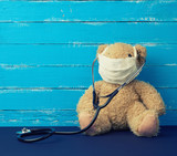 teddy bear is sitting in a white medical mask, black stethoscope is hanging on his neck