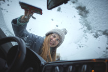 Girl With Emotional Face Cleaning The Windshield Of A Car From Snow.