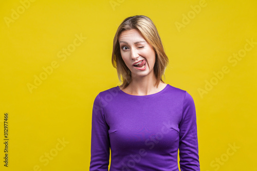 Fotografía Portrait of joyous playful woman in tight purple dress winking and sticking out her tongue, showing funny humorous face grimace, having fun at camera