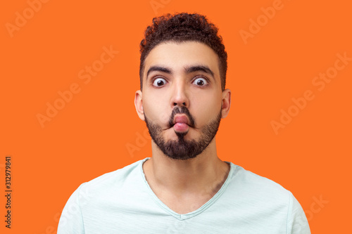 Cuadros en Lienzo Portrait of funny silly brunette man with beard in casual white t-shirt looking at camera and making fish face with lips and big eyes, fooling around