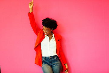 Portrait of a laughing young woman with arm up celebrating victory in front of a pink background