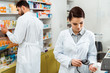 © LIGHTFIELD STUDIOS - Pharmacist scanning jar of pills with barcode scanner with colleague at background