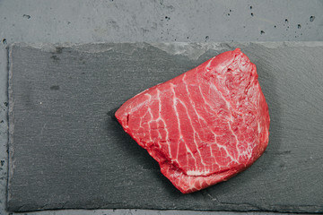 Raw beef, beef steak on a stone background. The concept of preparing a meal and eating. Fresh red beef, preparing a steak, using meat with a meal.