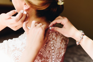 Bridesmaid helping bride fasten wedding dress