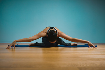 Sporty young woman doing stretching. Slim girl practicing yoga indoors on blue background. Calm, relax, healthy lifestyle concept.