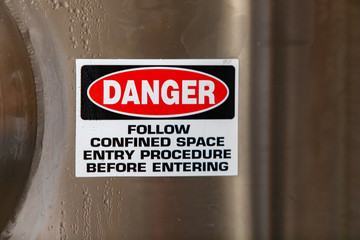 DANGER, FOLLOW CONFINED ENTRY PROCEDURE BEFORE ENTERING, warning vinyl sticker sign on stainless steel cold industrial tank, with copy space