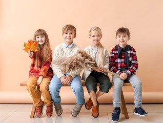 Canvas Print - Cute little children in autumn clothes sitting on bench near color wall