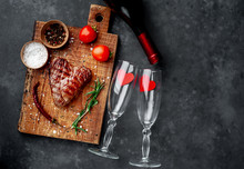 Grilled Beef Steak In The Form Of A Heart With Spices And A Bottle Of Champagne Or Wine With Two Glasses For Dinner For Valentine's Day On A Stone Background With Copy Space For Your Text