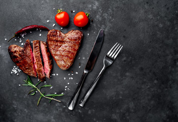 two grilled beef steaks in the form of a heart with spices for Valentine's day on a stone background with copy space for your text. dinner concept for two for Valentine's Day celebration