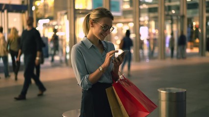 Wall Mural - Happy woman with purchase bags searching information about shopping sales received funny text message from friend, cheerful hipster girl reading positive news on fashion website and laughing