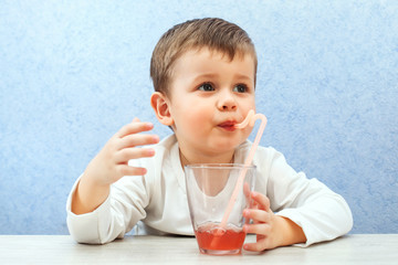 Cute little boy drinking juice on light blue background. Lovely kid drink grape juice.