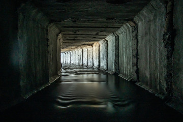 Wall Mural - light at the end of a turn in a square concrete rainwater or drain tunnel.