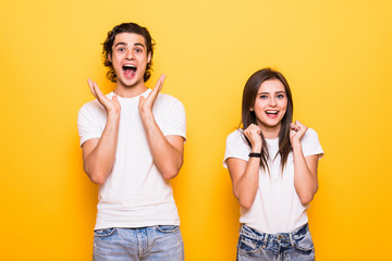 Excited couple two friends guy girl in white empty blank design t-shirts posing isolated on yellow orange background. People lifestyle concept. Keeping mouth open, spreading hands